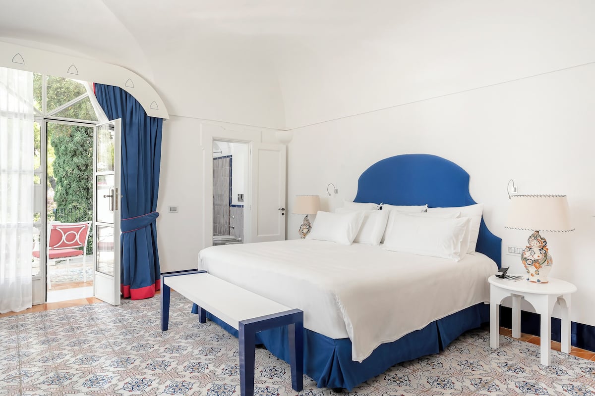 Un dormitorio con una cama grande, un banco, una mesita de noche y vistas al exterior.