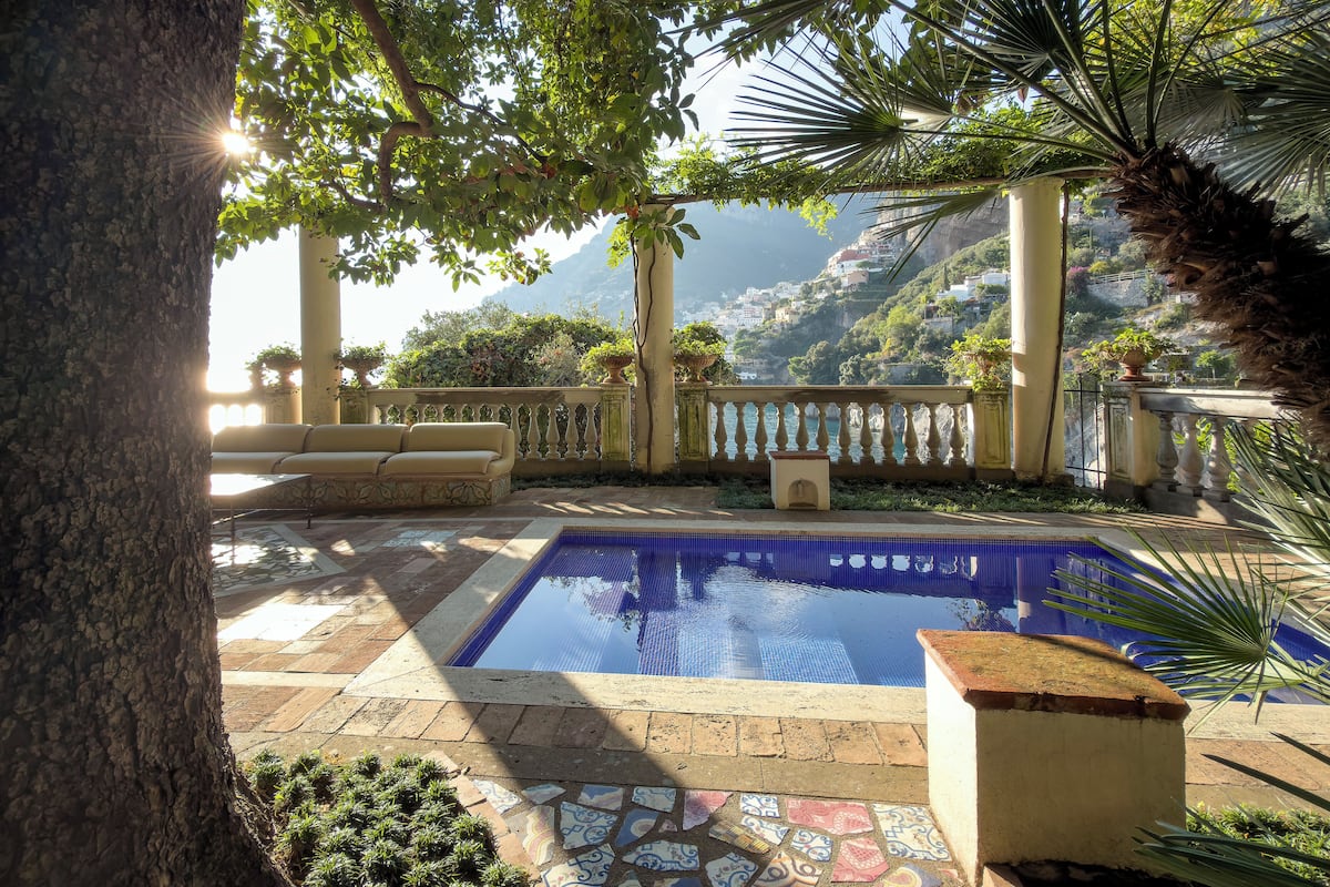 Zona de piscina con suelo de baldosas, un banco y vistas a un paisaje montañoso.