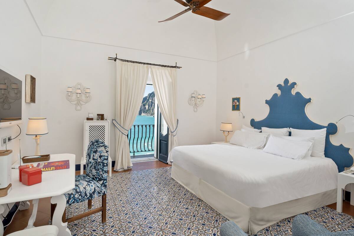 Habitación de hotel con una cama grande, un escritorio con lámpara, una silla y vistas al exterior.