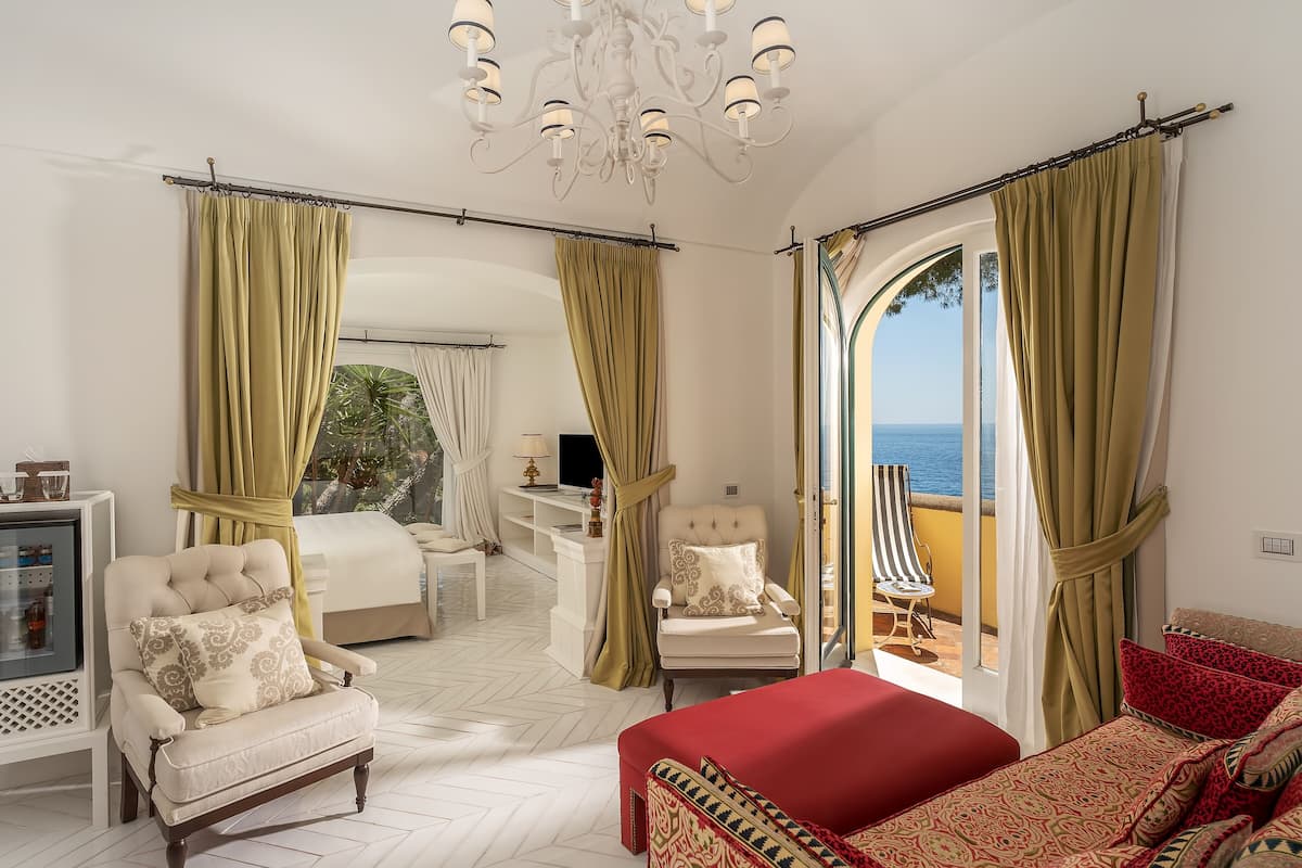 Un dormitorio amplio con una cama grande, un sofá rojo y una silla. Cuenta con un balcón con vistas al mar.