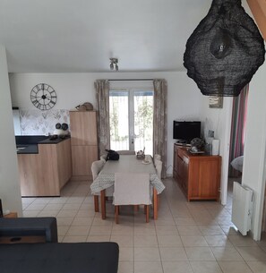 A compact living space with a dining area, kitchen, and a large black hanging light fixture.