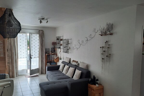 A modern living room with a sectional sofa, a hanging light fixture, and a decorative wall piece.