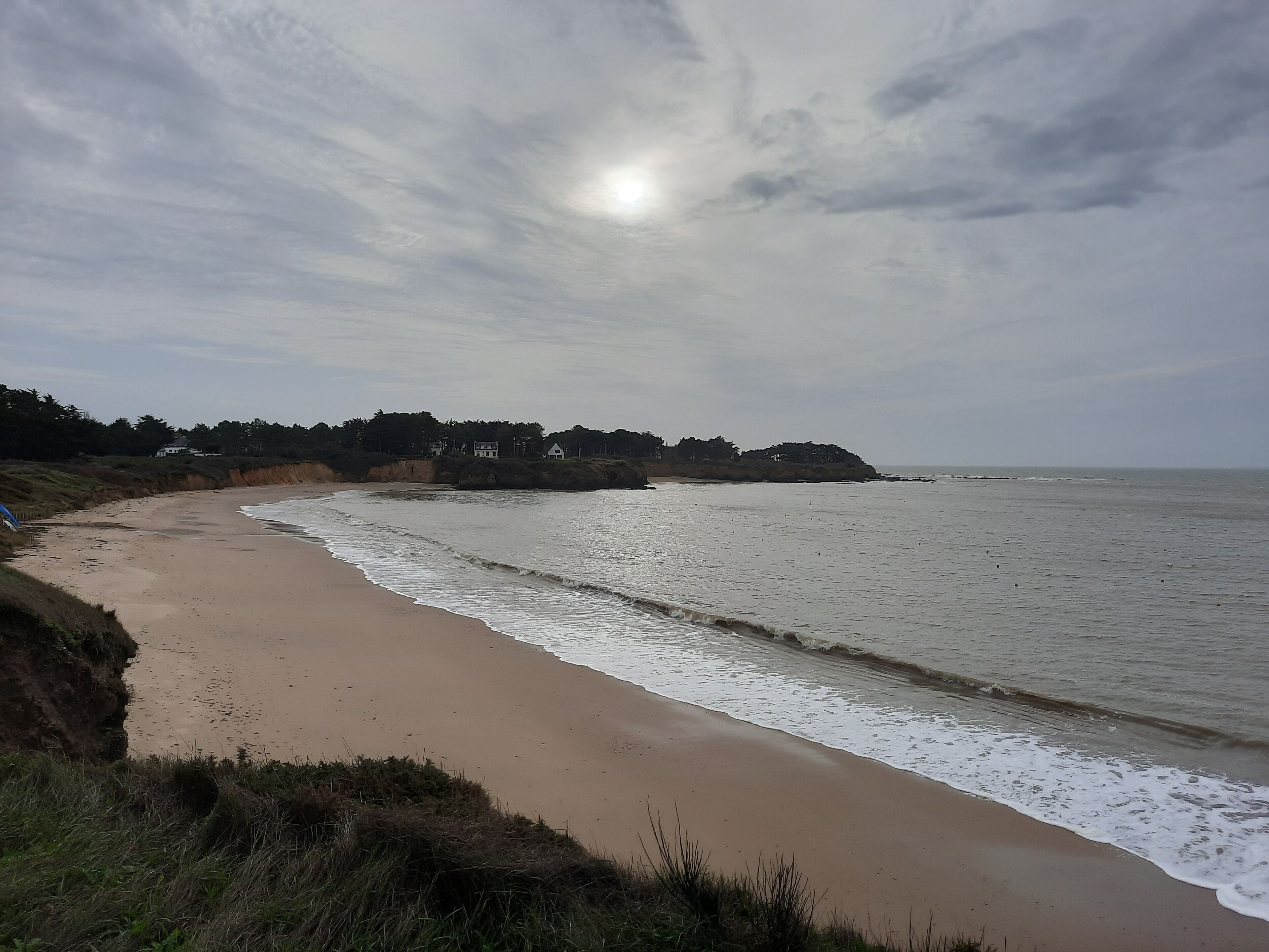 A beach with a sandy shore, waves, and a cloudy sky.