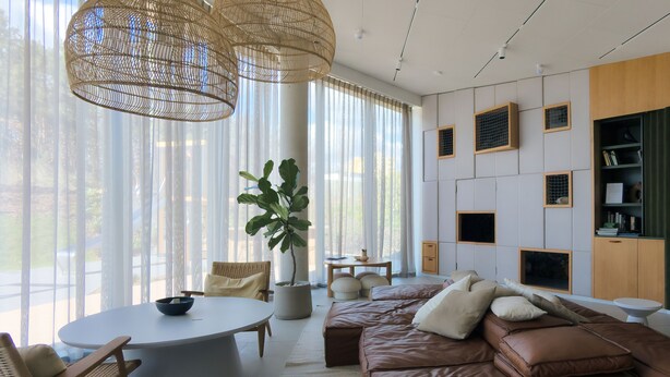 A modern living room with a brown leather sofa, a round white table, wicker pendant lights, and large windows with sheer curtains. - Gdańska 21R /5 (Gdansk)