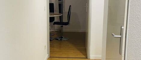 A narrow hallway with wooden flooring leading to a room with a dining table and chairs.