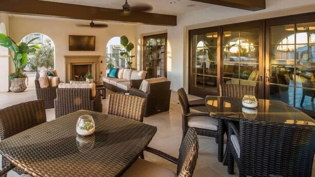A spacious outdoor area with wicker furniture, a glass table, and a fireplace.