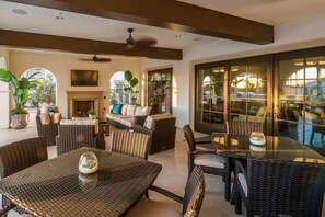 Un vaste espace extérieur aménagé avec des meubles en osier, une table en verre et une cheminée.