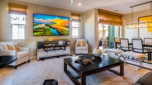 A spacious living room with a large flat-screen TV, comfortable seating, a coffee table, and a ceiling fan.