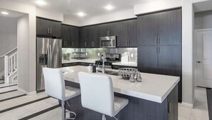 A modern kitchen with dark cabinets, stainless steel appliances, and a central island with bar stools.