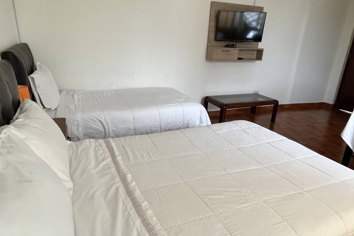 A hotel room with two beds, a TV mounted on the wall, and a small wooden table.
