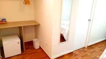A small, clean room with a wooden floor, a white wall, a mirror, a small white cabinet, and a wooden shelf with snacks.