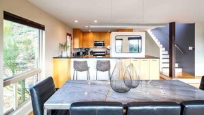 A modern kitchen with a central island, a dining area with a marble table, and a staircase leading to an upper level. - “Windmill House” -Mountain/City views, super close to great hiking trails (Phoenix)