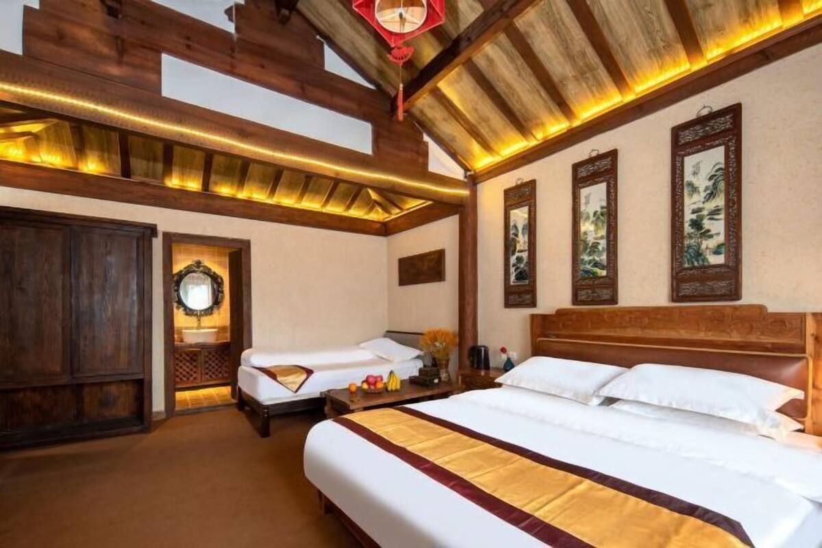 Quarto de hotel com uma cama grande, uma cama menor, vigas de madeira no teto e arte tradicional nas paredes.