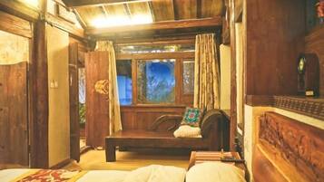 A wooden room with a bed, a bench, and a window with curtains.