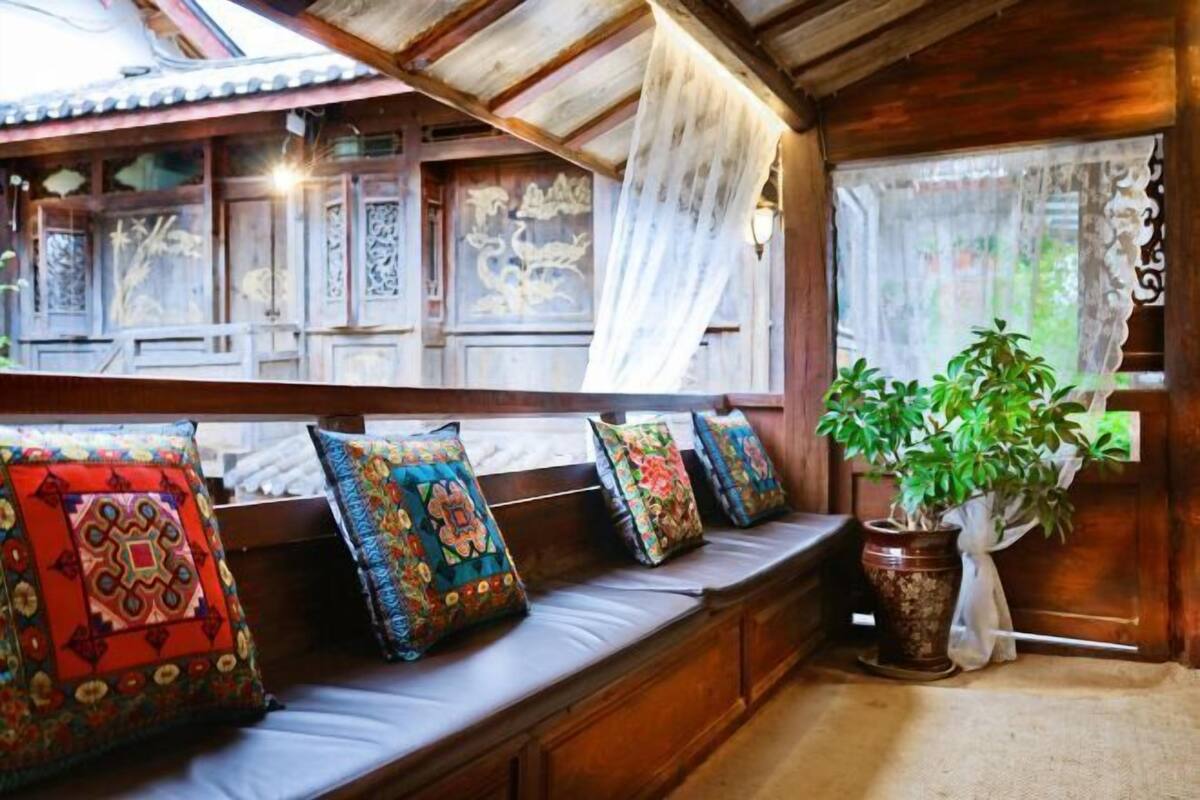 Interior de madeira tradicional com um banco, almofadas estampadas e um vaso de planta.