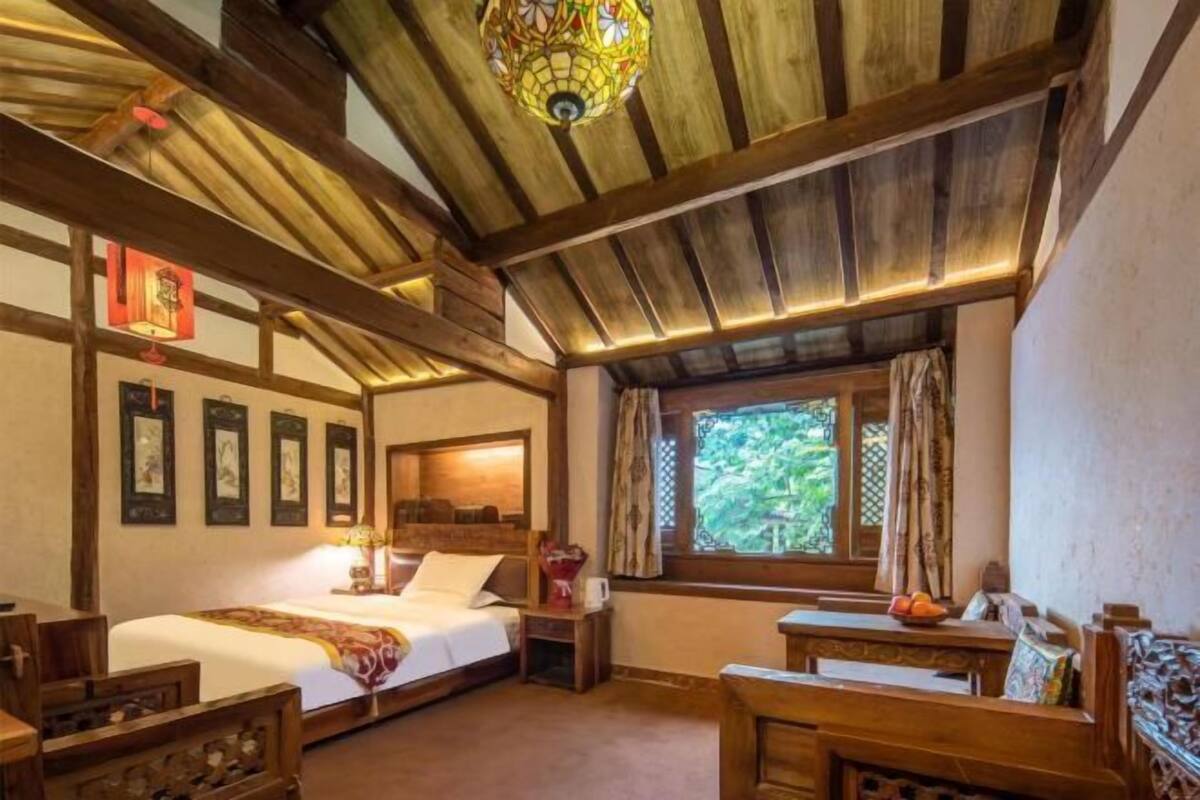 Quarto de madeira tradicional com uma cama, um banco de madeira e uma janela com vista para vegetação.