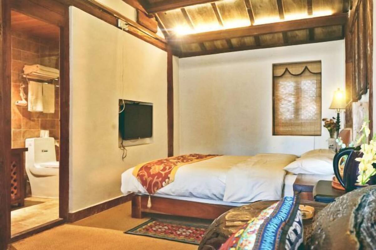 Quarto com cama, televisão, janela com cortina e banheiro com vaso sanitário e porta-toalhas.