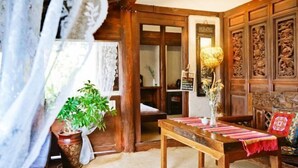 A traditional room with wooden furniture, a table with a cloth, a potted plant, and a wall with carved panels. - Lijiang Longfeng Villa (Shuhe Ancient Town Branch) (Lijiang)