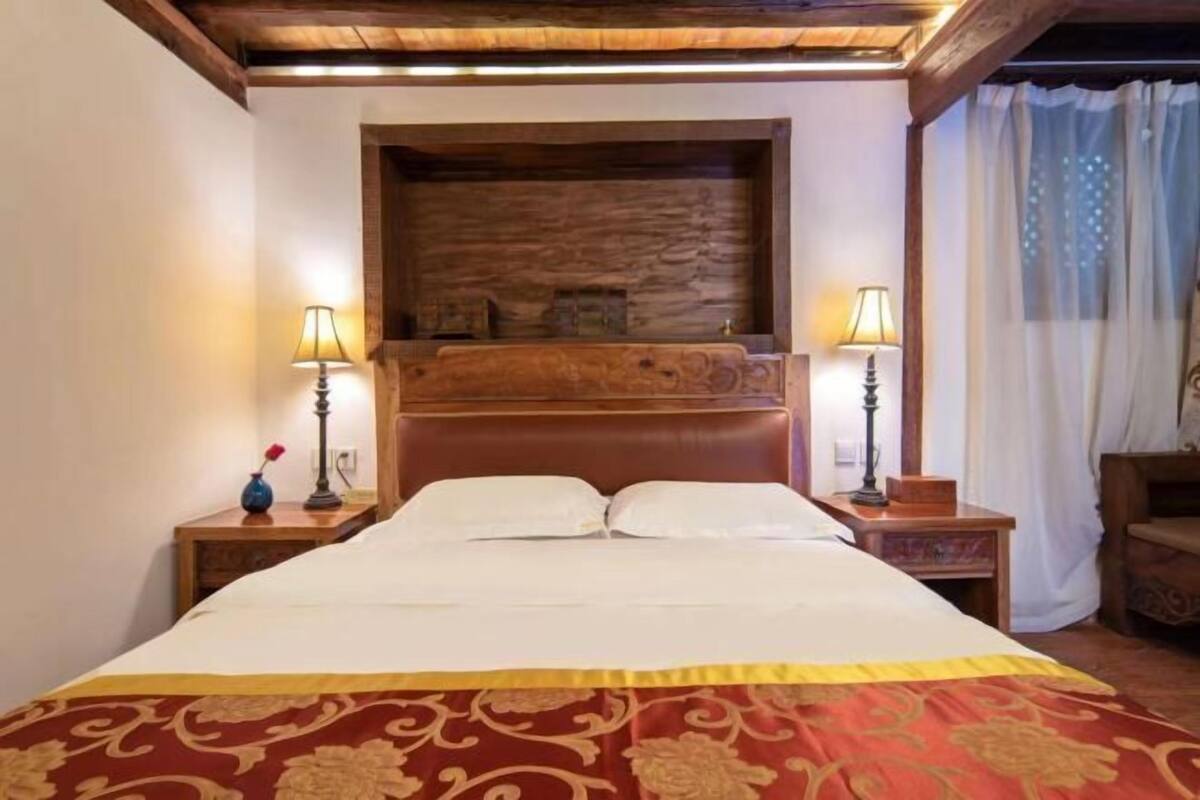 Uma cama com cabeceira de madeira, duas luminárias de cabeceira e um cobreleira decorativo.