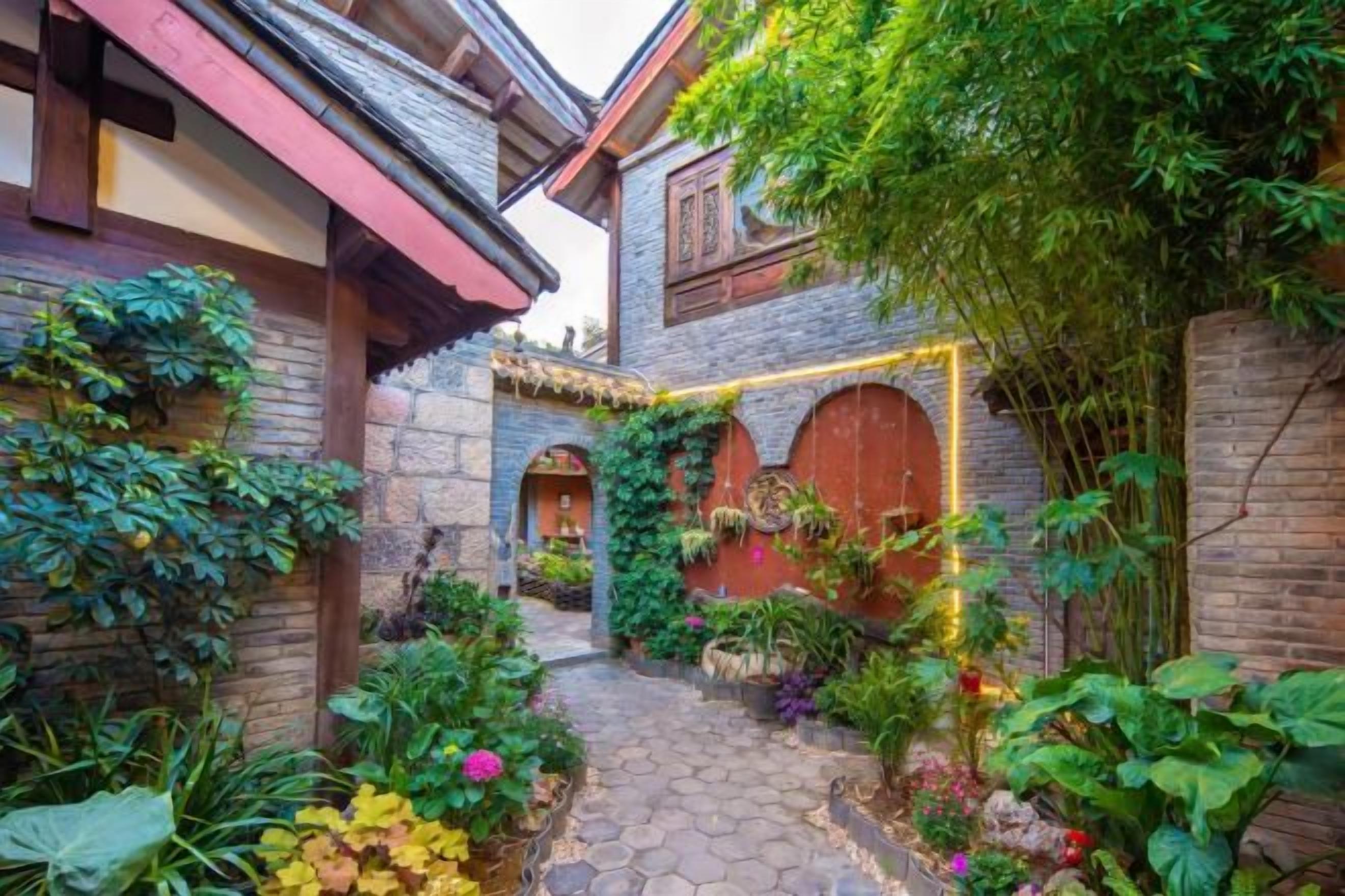 A courtyard with a cobblestone path, brick walls, and lush greenery.