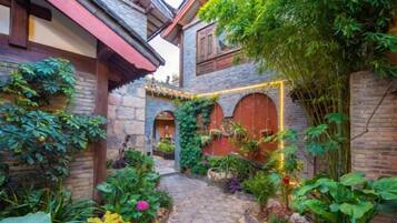 A courtyard with a cobblestone path, brick walls, and lush greenery.