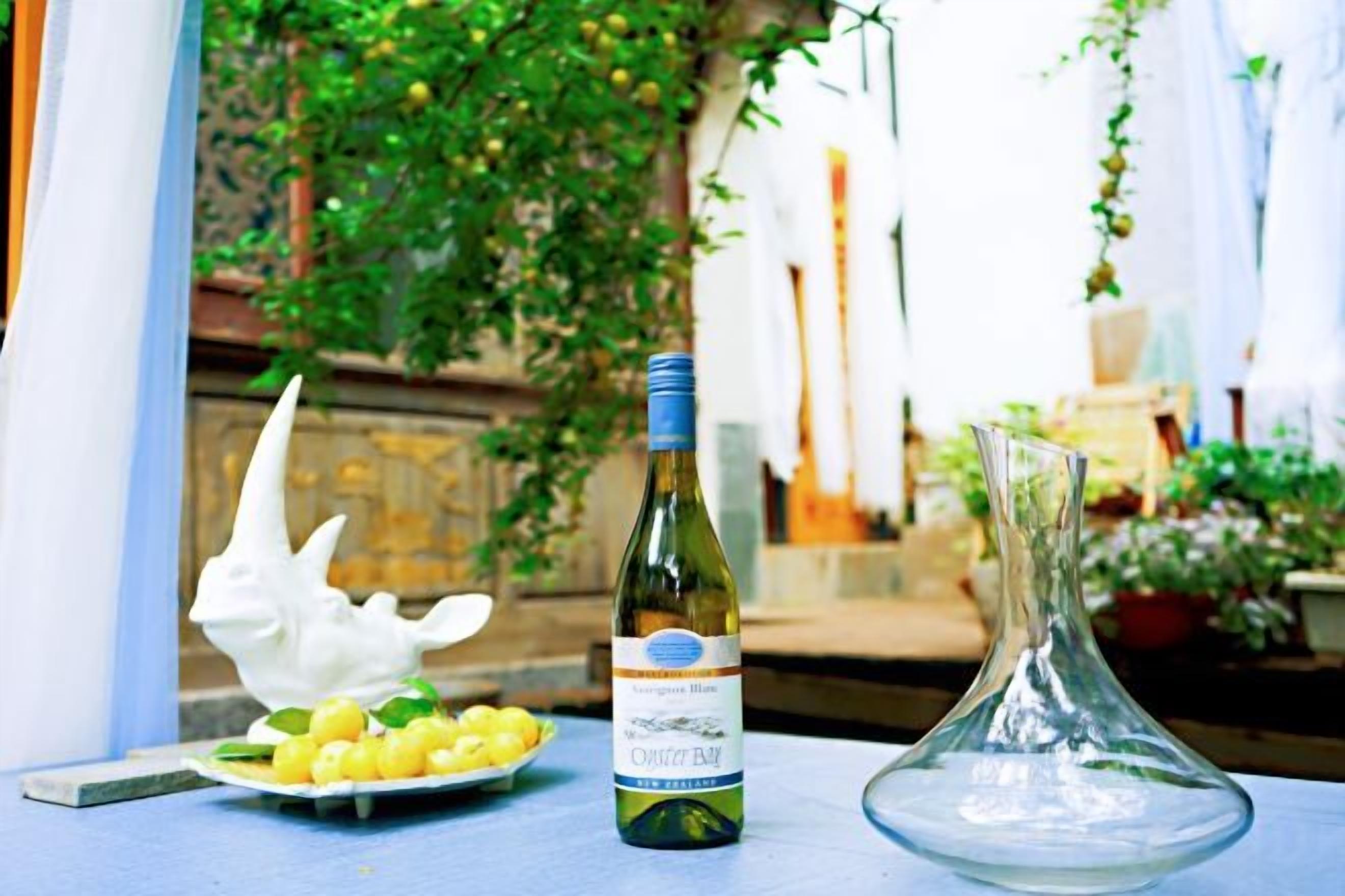 A bottle of wine, a plate of grapes, and a glass vase on a table.