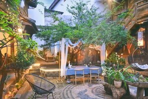 Un patio exterior con mesa y sillas, rodeado de macetas con plantas y un muro de piedra.