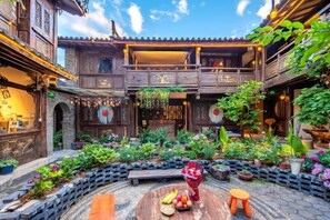 A courtyard with a wooden balcony, potted plants, and a round table with fruits and a vase. - Lijiang Longfeng Villa (Shuhe Ancient Town Branch) (Lijiang)