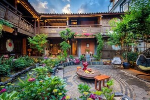 A courtyard with a circular seating area, potted plants, and a traditional wooden building with balconies. - Lijiang Longfeng Villa (Shuhe Ancient Town Branch) (Lijiang)