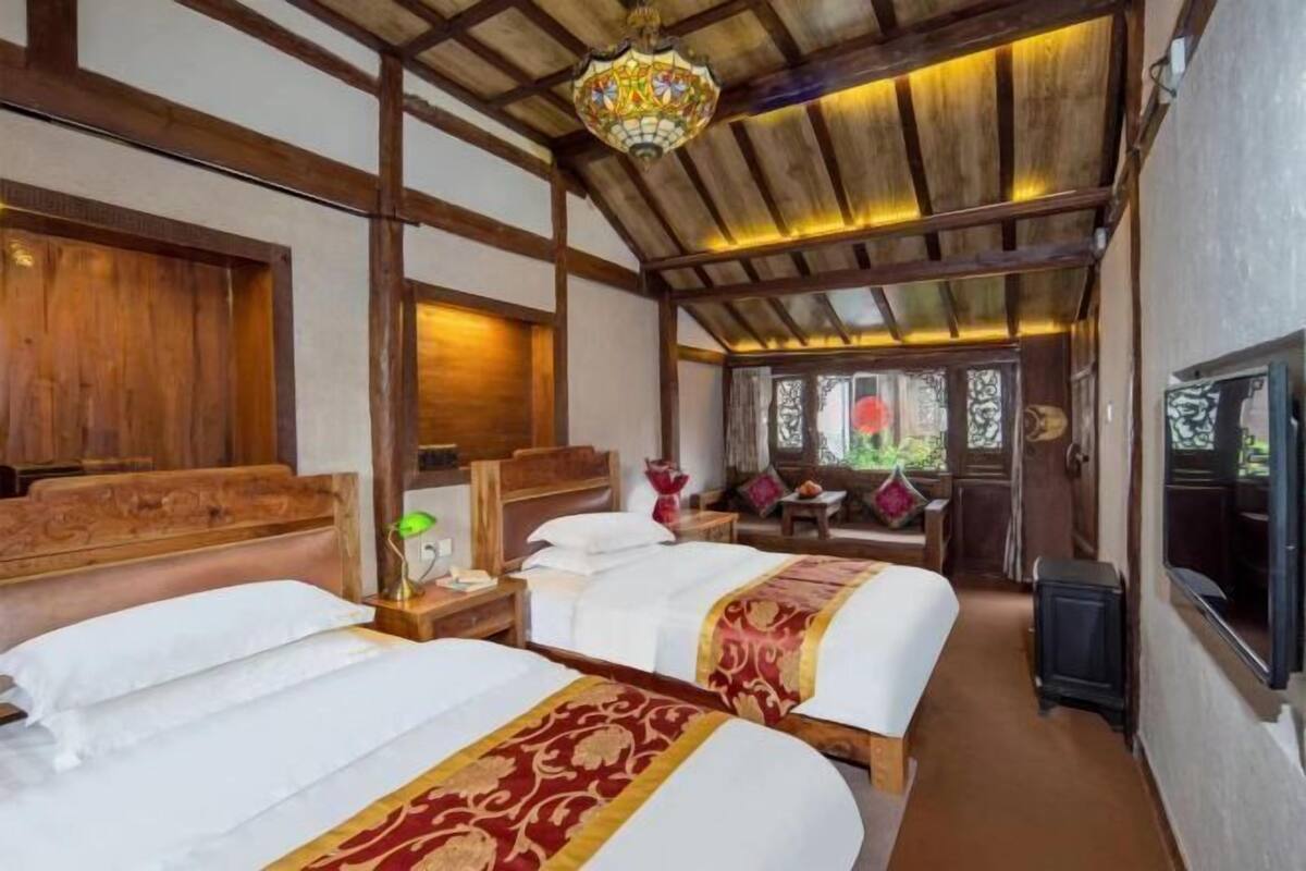 Quarto de hotel com duas camas, vigas de madeira, um candelabro e uma televisão.