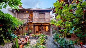 A traditional wooden house with a covered porch, a stone pathway, and lush greenery.