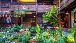 A traditional wooden building with a balcony, surrounded by a garden with various plants and flowers. - Lijiang Longfeng Villa (Shuhe Ancient Town Branch) (Lijiang)