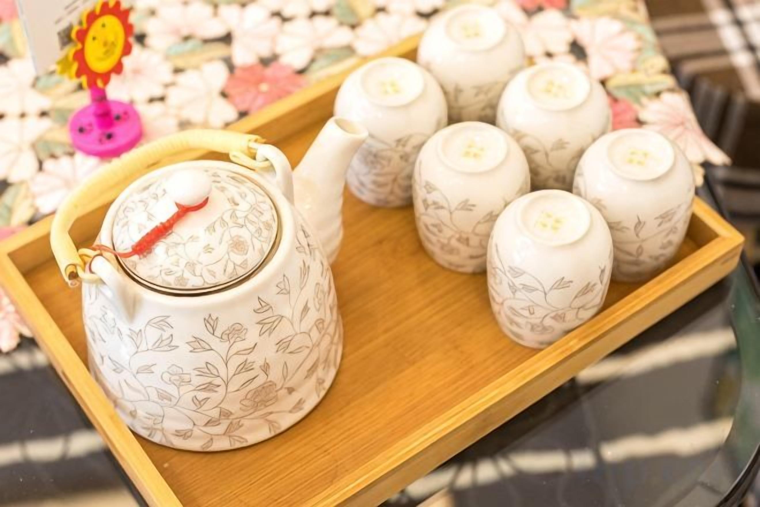 Una bandeja de madera con un hervidor de agua y varias tazas, todos decorados con motivos florales.