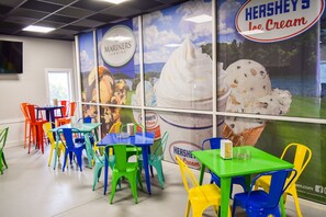 A dining area with colorful chairs and tables, a large Hershey's Ice Cream advertisement, and a window with a view of trees.