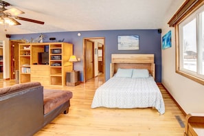 Un dormitorio con cama, un sofá, un aparador de madera con libros y una ventana.