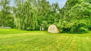 A well-maintained grassy yard with a wooden shed and a small structure, surrounded by dense trees and greenery. - Walkable to RIT/Comfortable Stay near university (Rochester)