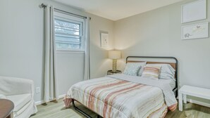 A bedroom with a bed, a bedside table with a lamp, a chair, and a window with curtains. - Walkable to RIT/Comfortable Stay near university (Rochester)