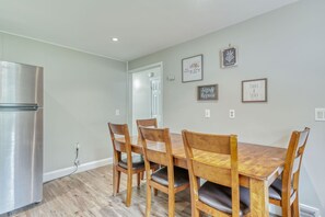 A dining area with a wooden table and four chairs, a stainless steel refrigerator, and a door leading to another room.
