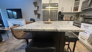 Cozinha moderna com uma ilha grande, piso de madeira escura, armários brancos e eletrodomésticos de aço inoxidável.