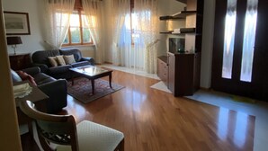 A spacious living room with a sofa set, a dining table, and a kitchen area with cabinets and a refrigerator.