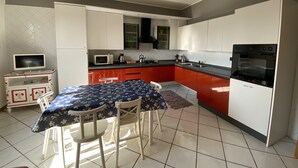 A compact kitchen with white and red cabinets, a microwave, a kettle, and a stove. There is a dining table with chairs and a television on a small cabinet.
