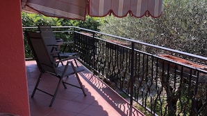 A balcony with a tiled floor, a metal railing, and a covered area with a striped awning.