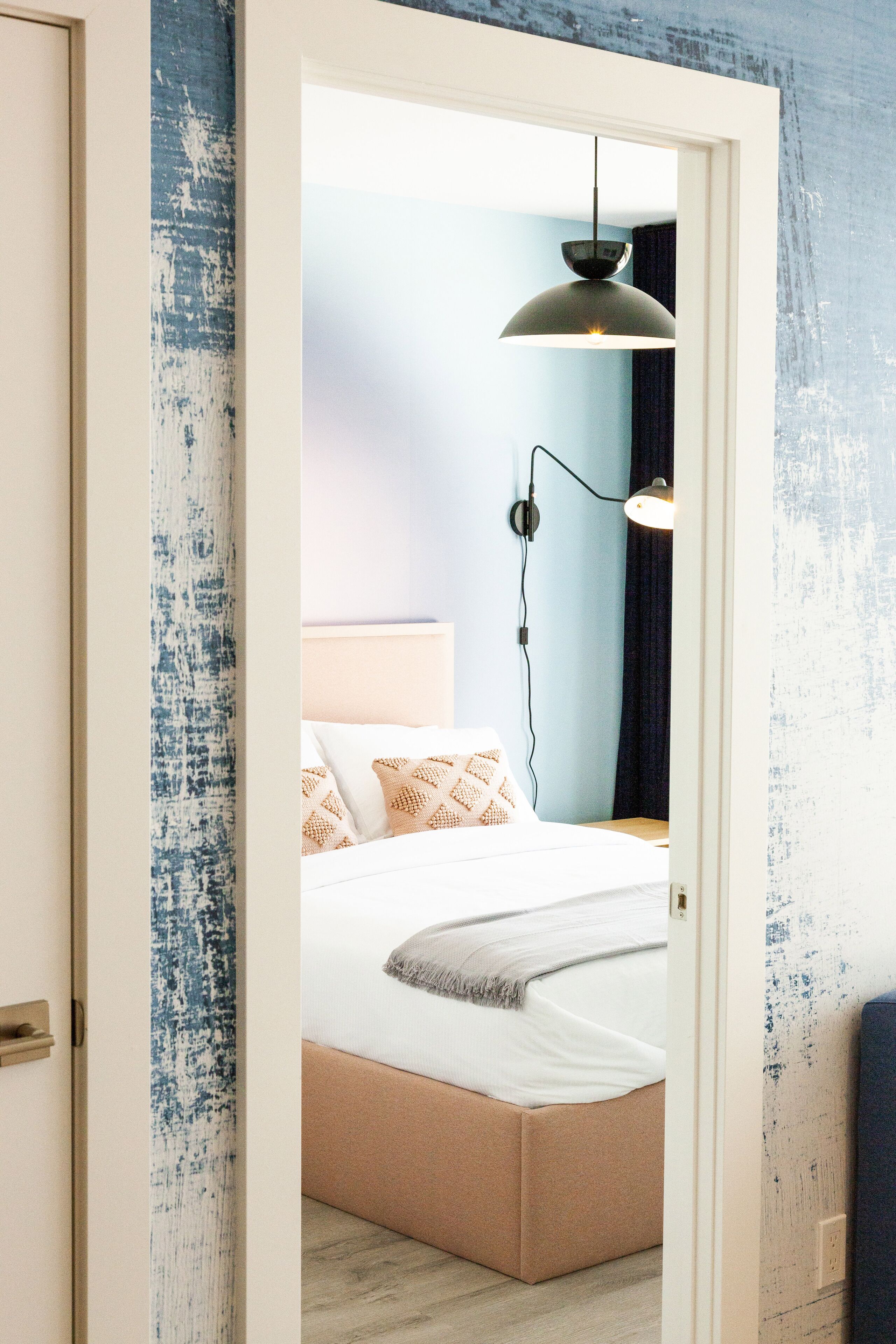 A bedroom with a bed, a bedside lamp, and a wall-mounted light fixture.