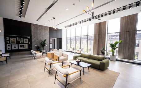 A modern lobby with a sofa, chairs, tables, and large windows offering views of the city.