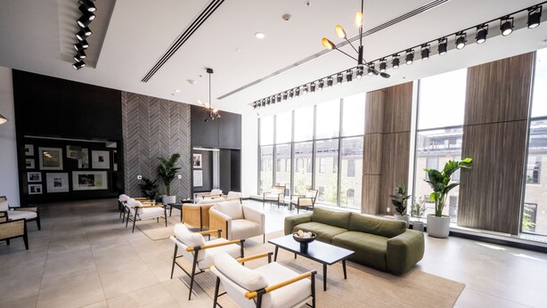 Een moderne lobby met een bank, stoelen, tafels en grote ramen met uitzicht op de stad.