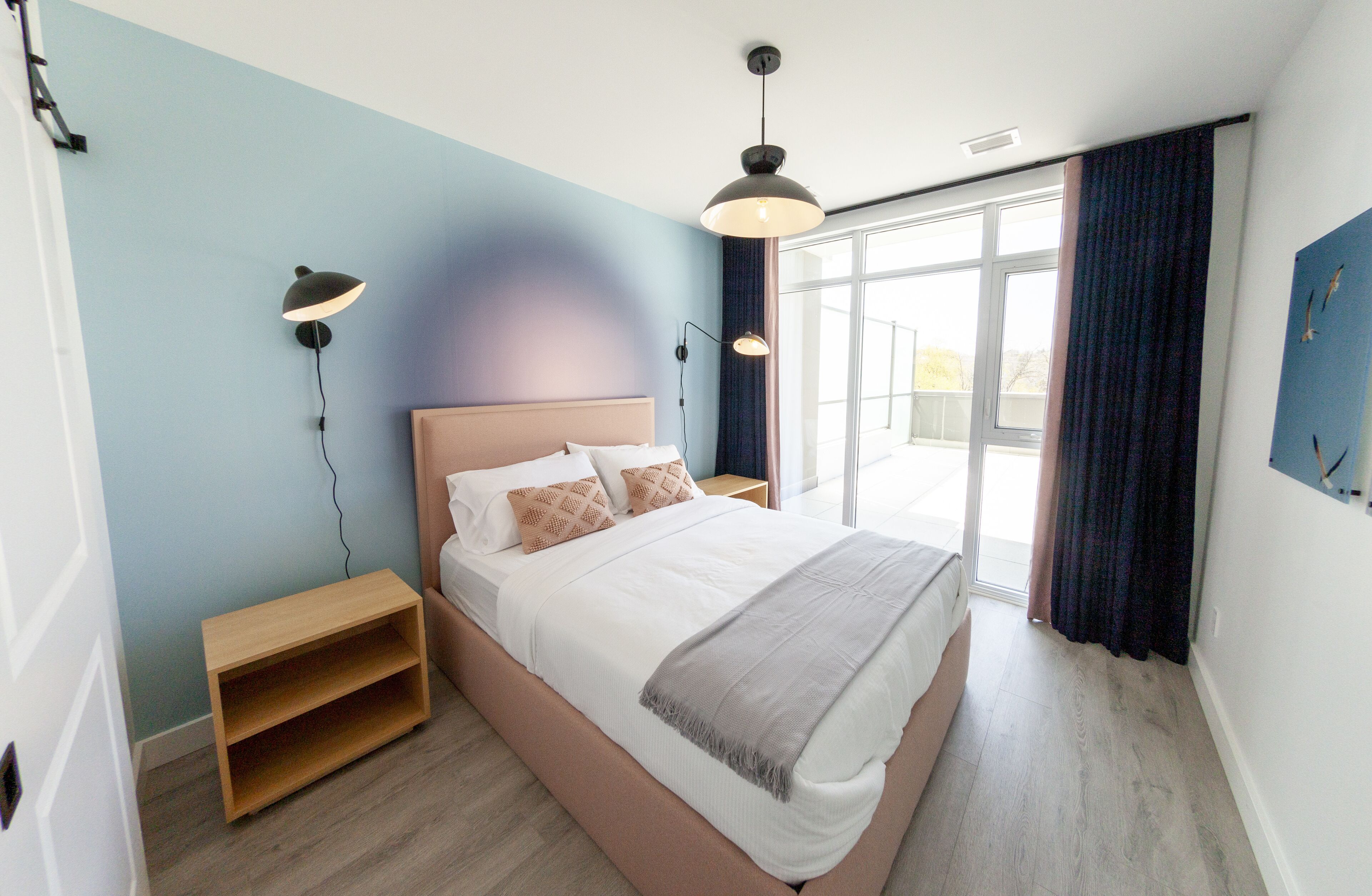 Quarto moderno com uma cama grande, luminárias de cabeceira, mesa de cabeceira de madeira e vista para o exterior por uma janela ampla.