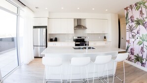 Een moderne keuken met witte kasten, een roestvrijstalen koelkast, een inbouwoven en een groot eiland met barkrukken.