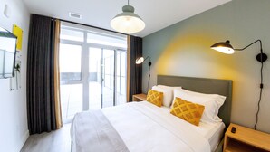 Een hotelkamer met een groot bed, twee bedlampen, een nachtkastje en uitzicht door een groot raam.