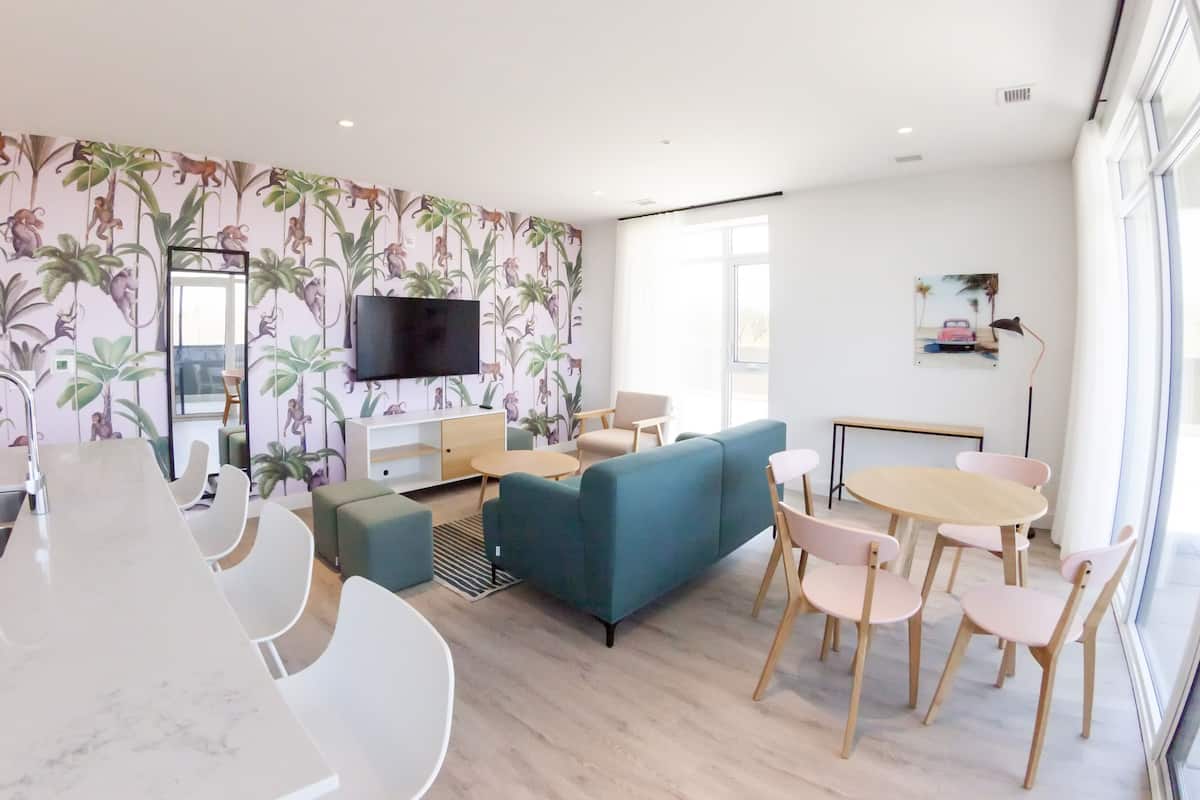 Uma sala de estar moderna com sofá, cadeiras, TV e área de cozinha com pia e bancada.