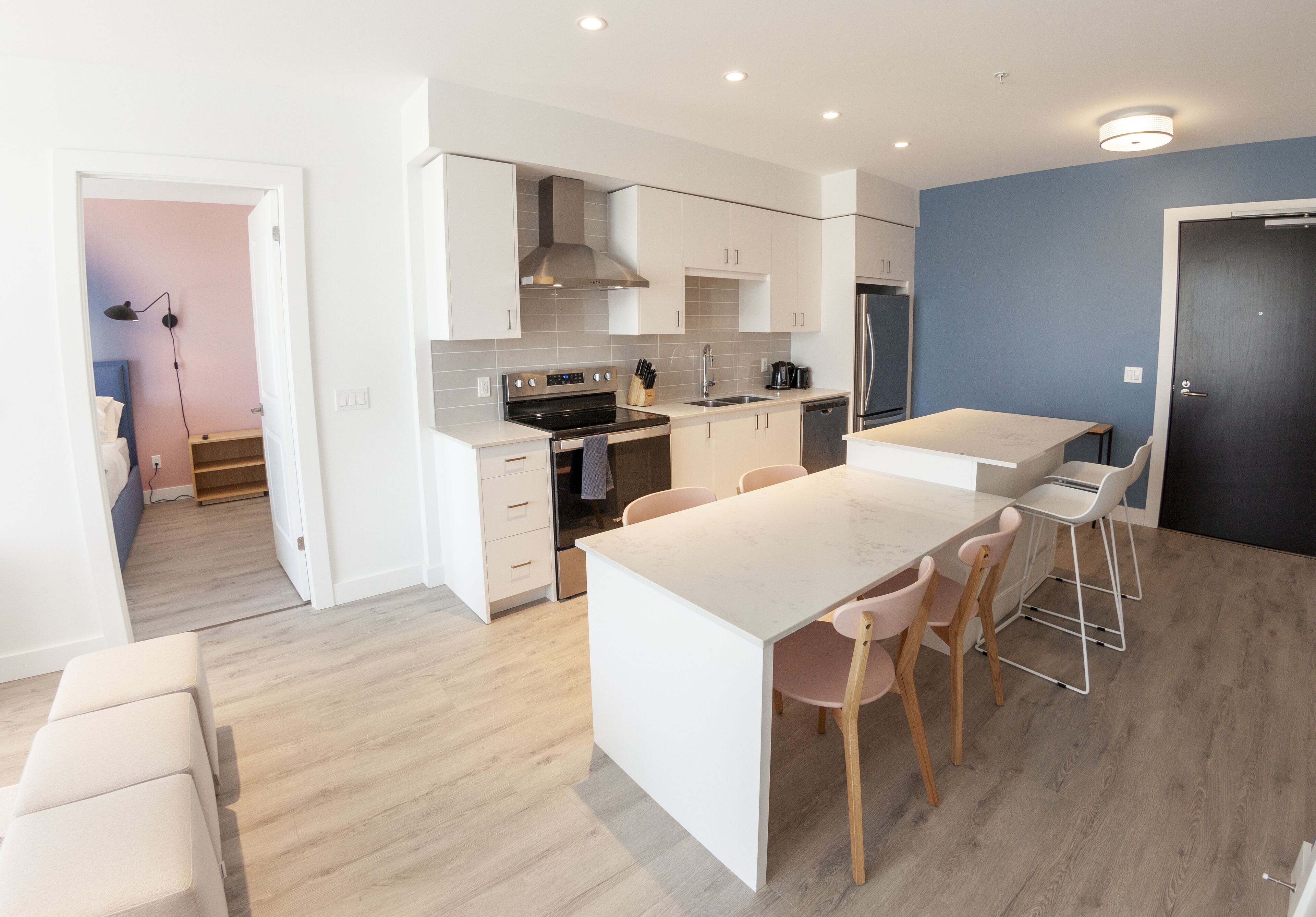 A modern kitchen with white cabinetry, a stainless steel refrigerator, and a dining area with a white table and wooden chairs.